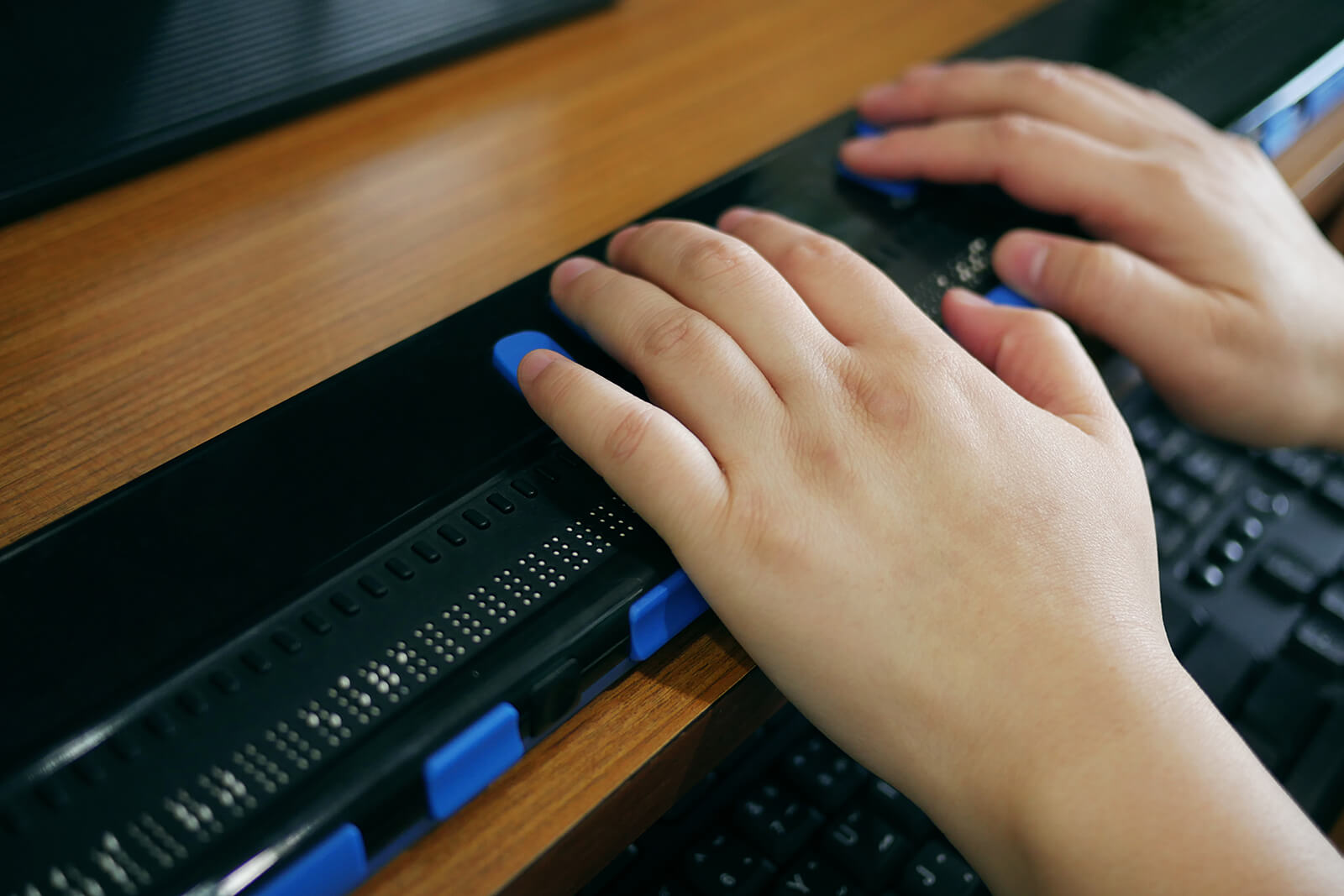 Close-up image of a persons hands using computer with braille display